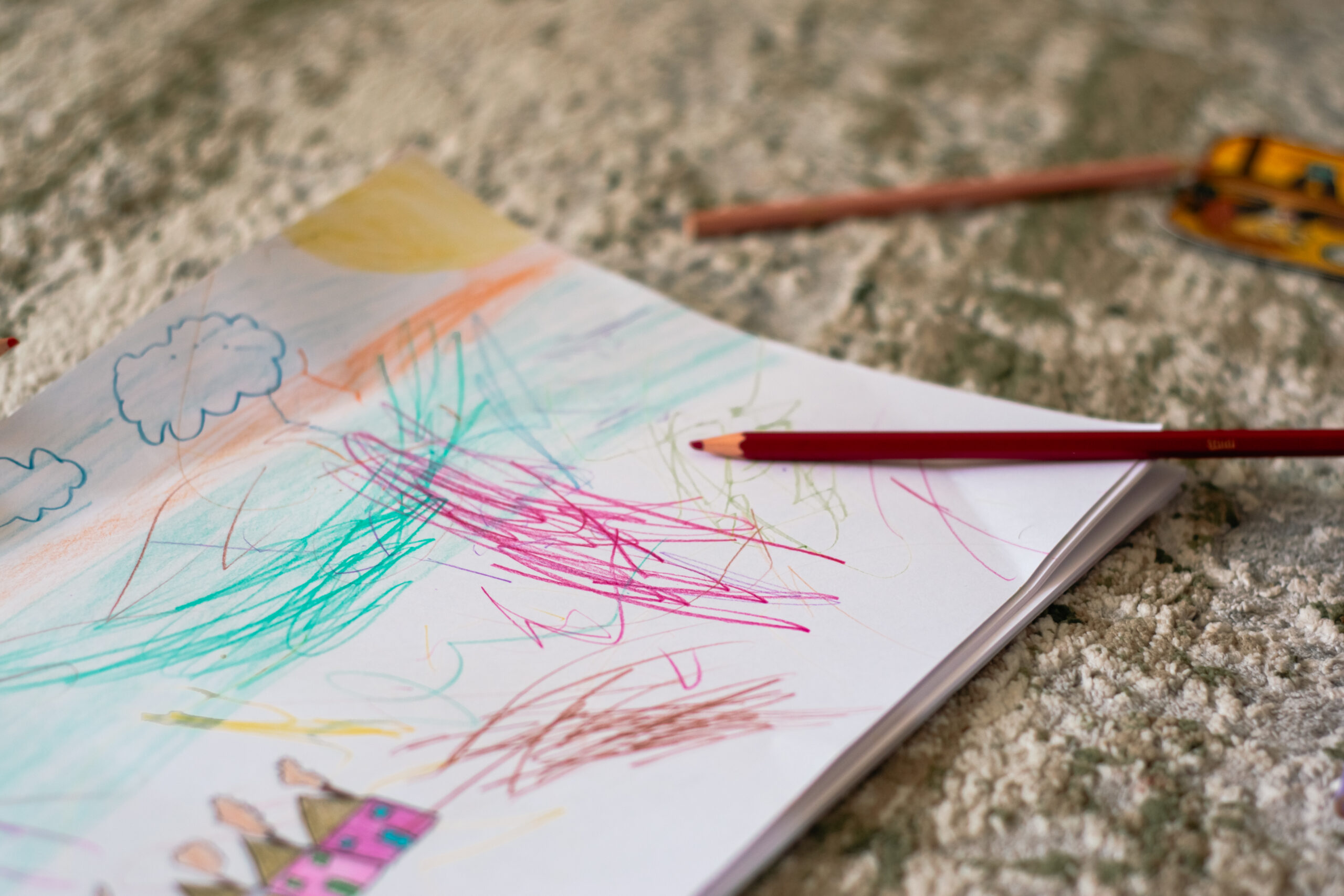 TUS A vibrant child's drawing on paper with colored pencils scattered on a carpet.