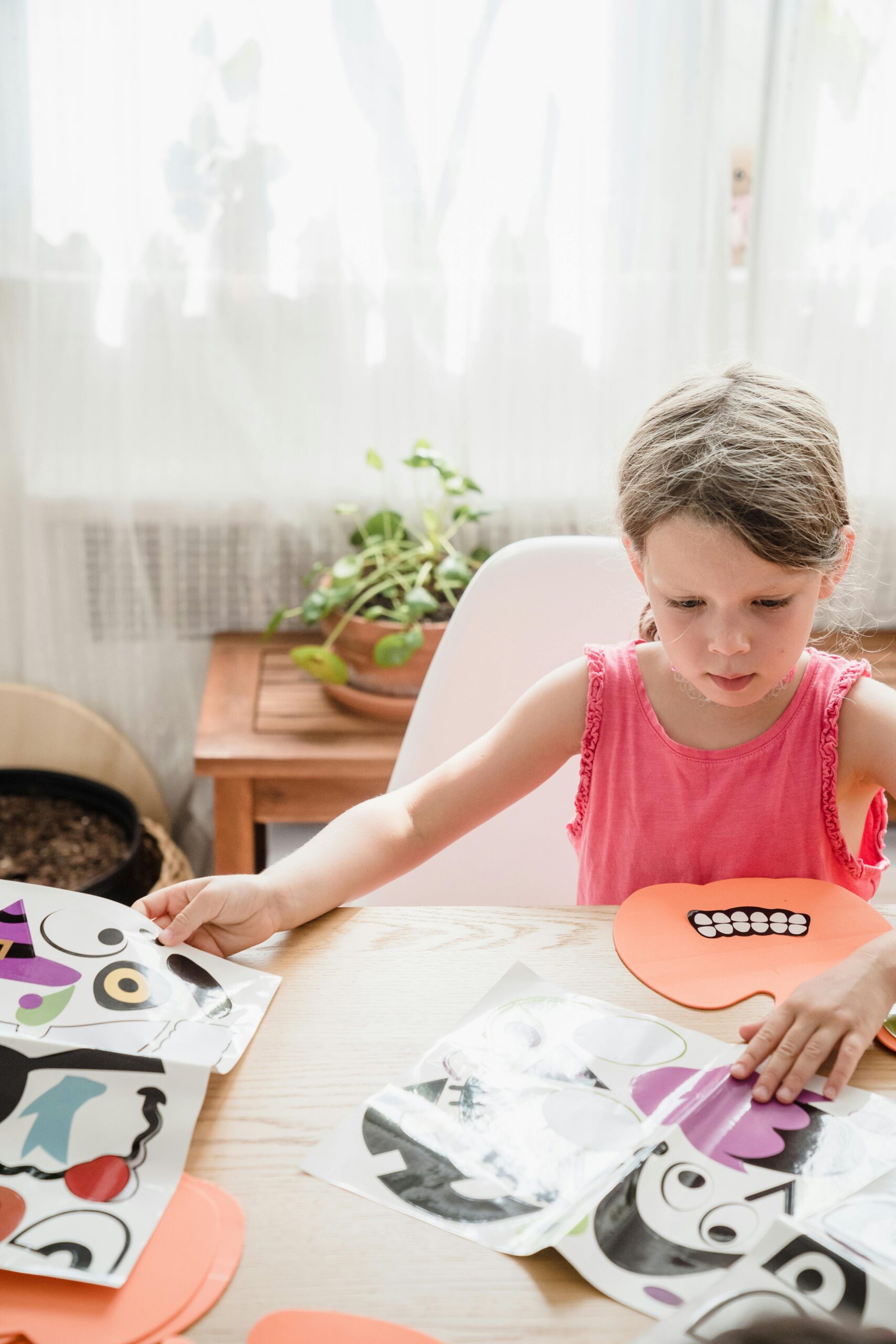 Young girl sitting indoors, playing with colorful paper cutouts, joyful craft time.